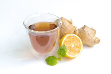 transparent glass with tea and fresh ginger root with lemon and mint or melissa leaves on a white isolated background