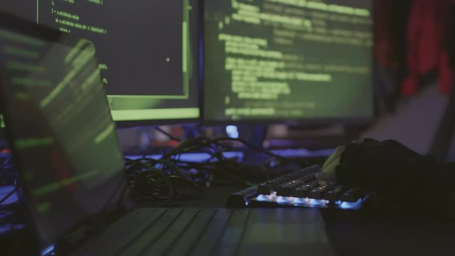 Close up of hands of unrecognizable coder sitting in dark room and developing program code on different computers