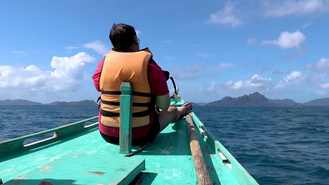 A male tourist sitting on the end of the boat, enjoying the sunlight and the scenery at El Nido Palawan, Philippines.
