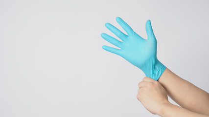 Left hand is pulling right hand wearing blue latex gloves on white background.