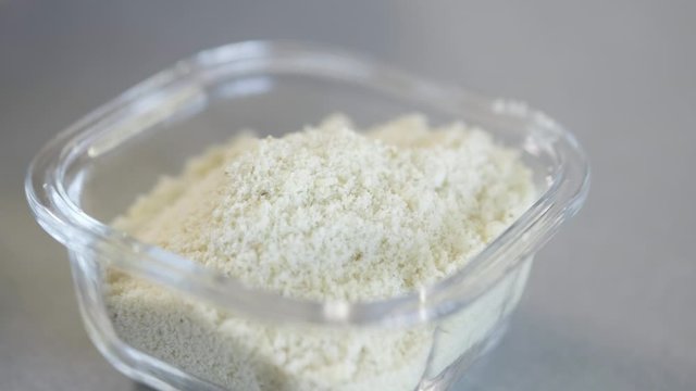 Grated cheese stored in a see through open square container on grey kitchen top
