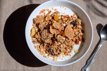 white plate with milk or yogurt and cereal, a healthy rustic breakfast, bright sunshine