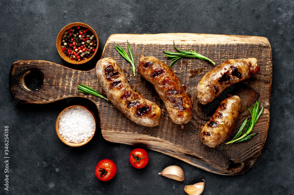 Wall mural grilled sausage with spices and rosemary on cutting board on stone background