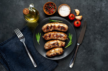 grilled sausages with spices and rosemary in a black plate on a stone background