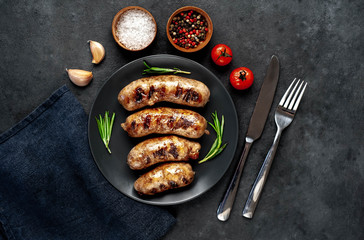 grilled sausages with spices and rosemary in a black plate on a stone background
