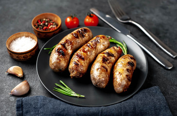 grilled sausages with spices and rosemary in a black plate on a stone background