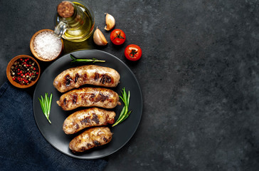 grilled sausages with spices and rosemary in a black plate on a stone background with copy space for your text