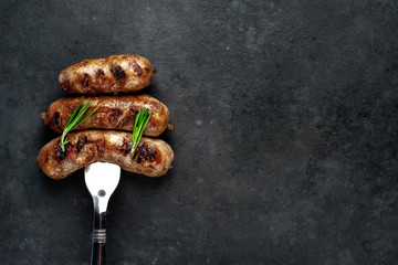 grilled sausages with spices on a meat fork on a stone background with copy space for your text