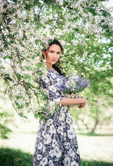 Girl with a bouquet of lilacs. A beautiful woman in a summer dress under a cherry blossom. A young girl against the background of spring flowering trees. Romantic lady in a blooming garden