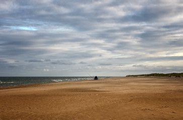 Lonley fisherman isolated on a big sandy beach