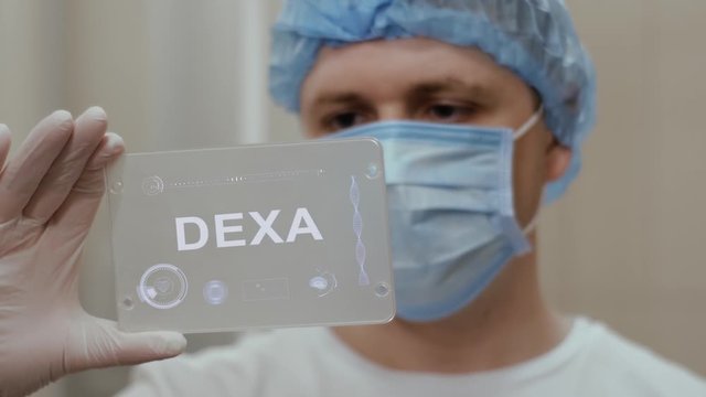 Doctor in face mask interacts futuristic hud screen tablet with text Dexa. Medical concept of future technology. Futuristic doctor with modern medical care gadget