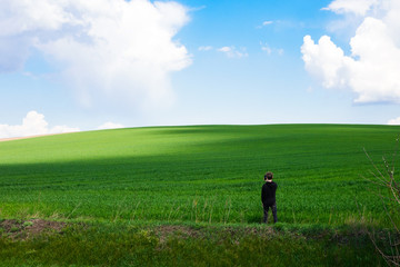 A young man in black clothes on a field of green young wheat shoots a picturesque landscape. Travel Ukraine.