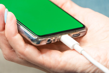 Woman hands plugging a charger in a smart phone with green screen. Phone Connected to charger