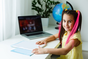 Cool online school. Kid studying online at home using a laptop. Cheerful young little girl using laptop computer studying through online e-learning system. Distance or remote learning