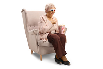 Elderly woman with 3d glasses sitting in an armchair eating popcorn