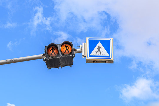 Urban view. Pedestrian worker lighted traffic light. A blue road sign is hanging nearby. Against the background of a bright bright sky. View from the bottom up. Protection concept. Copy space. © Nikolay