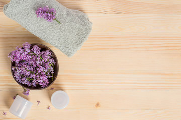 Obraz na płótnie Canvas Spa, body and skin care with cosmetic bottles, towel and lilac flowers in a coconut bowl on a wooden table. Banner, beauty concept