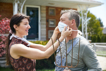 A wife lovingly ties a coronavirus facemask on her husband before work to prevent exposure to the virus