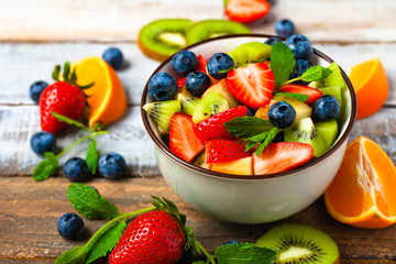 Concept of low calories delicious desserts. Summer fresh bowl with colorful fruit salad. Healthy natural organic food. Tasty sweet snack, light simple tasty lunch. Close up macro view wooden backgroun