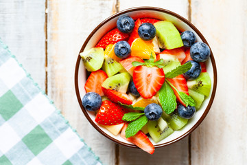 Concept of low calories delicious dessert. Summer fresh bowl with colorful fruit salad. Healthy natural organic food. Tasty snack, light simple lunch. Close up, wooden background, flat lay top view