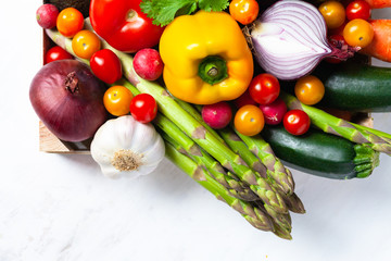 Wooden case with fresh ripe seasonal vegetables. Ingredients for cooking tasty light vegan meal. White background, close up, macro. Top view flat lay