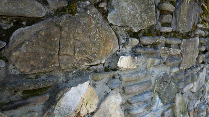 Fragment of a wall from a chipped stone at sunny day. The stones are arranged into layers of stone walls.