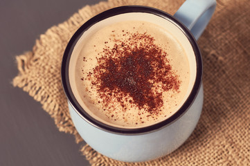 Blue mug of coffee with foam on sackcloth and concrete surface. Concept of love or christmas. Toned and vintage image
