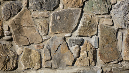 Fragment of a wall from a chipped stone at sunny day. The stones are arranged into layers of stone walls.