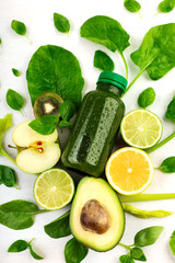 A creative vertical composition of bottle filled with green beverage laying among variety of sliced froitsand vegetables on a white background.