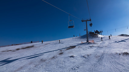 Top of mountain against blue sky at sunny day in the Carpathians. Ski lift is lifting people to top of mountain.
