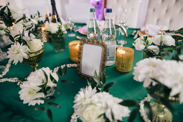 golden photo frame stands on the festive table, there are also candles, cutlery and fresh flowers