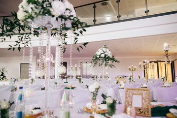 Wedding banquet tables decorated with a composition of white flowers and greenery, there are cutlery and candles