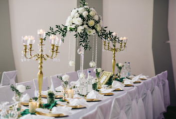 Festive table served dishes and decorated with branches of greenery, flower compositions and candlesticks, stands in the area of wedding party