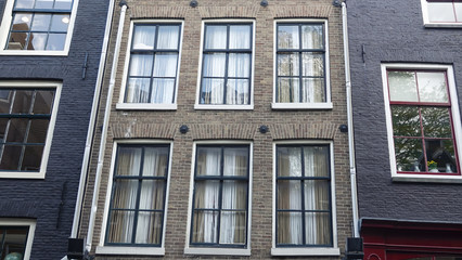Fototapeta na wymiar Looking up at the typical facade of houses with large traditional windows at old street of Amsterdam. Close up