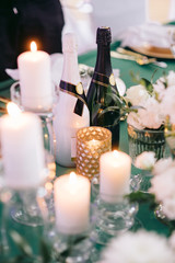 Wedding table decorated with flowers, candles, greenery, bootles of champagne and with green tablecloth