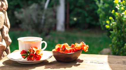 white porcelain cup with tea and red quince flowers on a wooden table in the garden