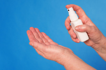 Eldery caucasian doctor lady in white coat and with stethoscope on blue background. Close up of using antiseptic
