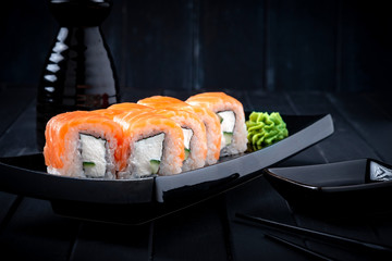 Philadelphia roll set with salmon, cucumber and cream cheese on a Japanese plate on a black wooden background with chopsticks and soy sauce