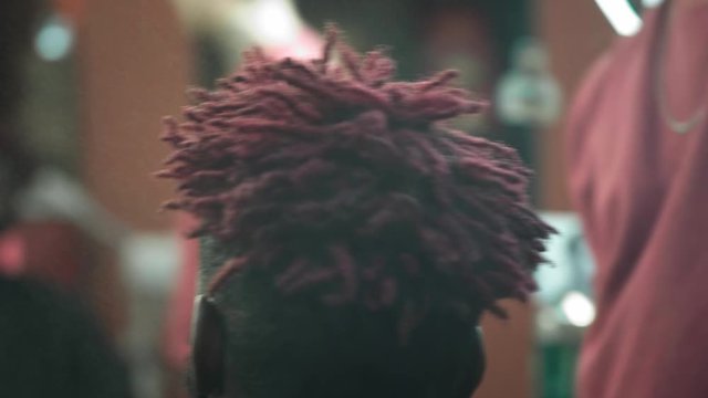 Hair Salon. Barber sprays a special liquid or water on the hair of a client at the hairdresser. Spray drops on red dreadlocks of an African American. Hair gets wet