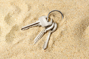 Ring with three home keys on a sea sand. Forget or fall house keys while relaxing on the beach. Accidentally drop keys. Lose bunch of apartment keys concept.