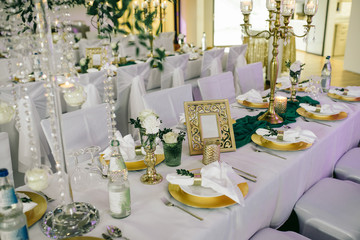Compositions of flowers and greens, candles, cutlery, plates with napkins, two bottles of champagne on the festive table