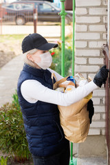 Woman delivering food in paper bag during Covid 19 outbreak.Feme volunteer holding groceries in the house porch.Volunteer in the protective medical mask and gloves