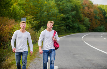 Obraz premium Tourist traveler travel auto stop. Transporting issues. Pick spot where car can easily pull aside. Men backpack walking road. Twins walk along road. Adventure concept. Guys hitchhiking on road
