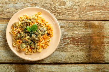 Pasta with mushrooms in a creamy sauce with spinach on a wooden table. Copy space.