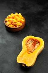 Pumpkin half, fresh pieces in wooden bowl on black background. Cutted raw butternut squash