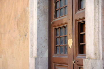 Fototapeta na wymiar Rome, Italy - February 24, 2012: .Ancient brown wooden door of one of the old houses of Rome. There is a window with bars on the door. Heart sticker on the door