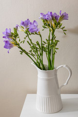 Purple freesia flowers at white vase.