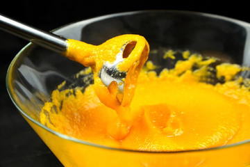 Pumpkin puree with blender in transparent bowl on black background. Cooking mashed pumpkin