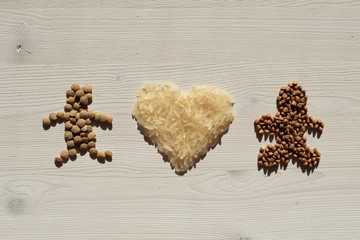Two little men made of lentils and buckwheat with a heart of rice on a white wood background