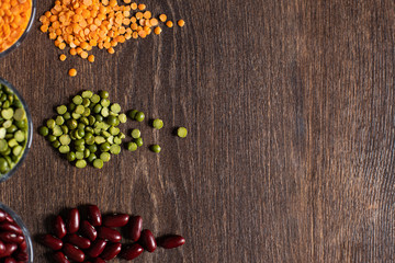 three types of legumes, beautifully laid out in cups and on a wooden background - red beans, green peas and orange lentils. Top view. copy space.